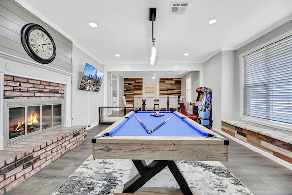 A pool table in a modern living room with a fireplace, a clock, and a cityscape painting.