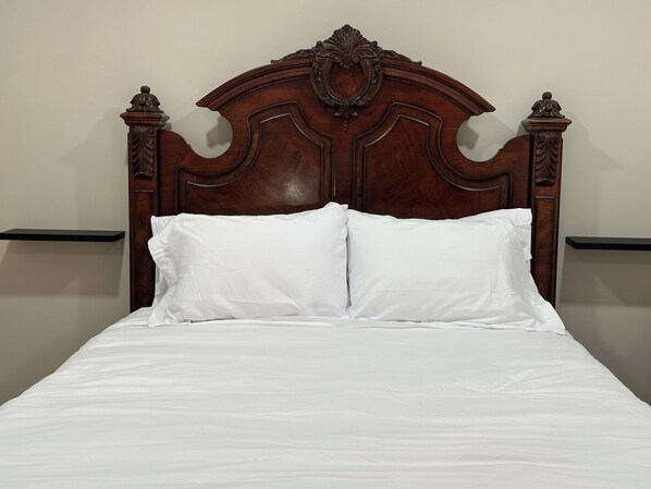Una cama bien hecha con un cabecero de madera, ropa de cama blanca y dos mesitas de noche con cómodas negras.