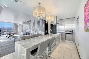 A modern kitchen with a marble countertop, stainless steel appliances, and a dining area with a pool table.