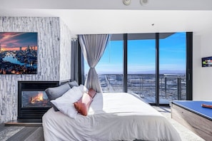 A modern bedroom with a cityscape view, a fireplace, and a large bed.