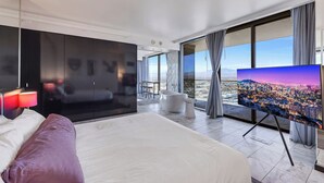 Una camera d'hotel moderna con un letto grande, una televisione a schermo piatto, vista sulla città e un balcone.