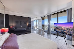 Una habitación de hotel moderna con una cama grande, televisión de pantalla plana, vista a la ciudad y un balcón.