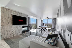 A modern living room with a flat-screen TV, a fireplace, a pool table, and a sofa with colorful cushions.
