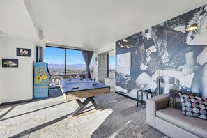 Ein Zimmer mit Tischtennisplatte, einer Couch, einer Wand mit großem abstrakten Gemälde und Blick auf die Stadt durch große Fenster.
