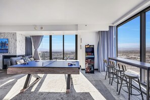 A modern hotel room with a ping pong table, a gaming console, and a city view.