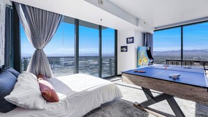 Camera d'hotel di un grattacielo con un letto, un tavolo da ping pong e vista sulla città.