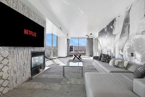 A modern living room with a flat-screen TV, a fireplace, a sofa, and a dining area with a view.