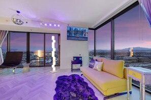 A modern living room with a city view, a sofa, a chair, a decorative floor lamp, and a flat-screen TV.