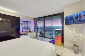 Une chambre dâhĂŽtel moderne avec un grand lit, un canapĂ©, une vue sur le paysage urbain et un tableau au mur.