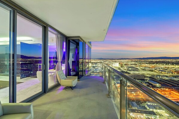 Un balcon avec vue sur la ville, une chaise et une rambarde en verre.