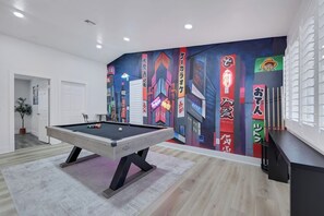 A pool table in a room with a vibrant wall mural, a potted plant, and a door.