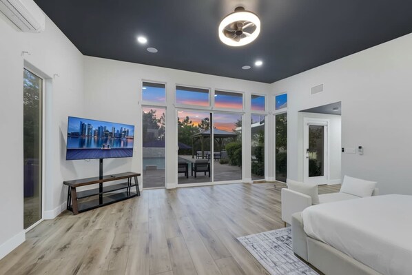 Une chambre moderne avec un grand lit, un tĂ©lĂ©viseur fixĂ© au mur et une vue sur lâextĂ©rieur grĂące Ă des portes vitrĂ©es.