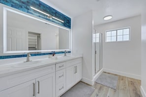 A modern bathroom with a large mirror, two sinks, and a walk-in shower.