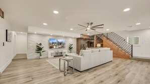 Ein modernes Wohnzimmer mit einem weißen Sofa, einem kleinen Beistelltisch, einem Fernseher und einer Treppe.