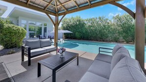 Ein überdachter Außenbereich mit Pool, Sitzgelegenheiten und Blick auf ein modernes Gebäude.
