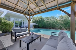 A covered outdoor area with a pool, seating, and a view of a modern building.