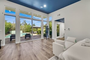 Une piĂšce spacieuse dotĂ©e dâune grande porte-fenĂȘtre coulissante donnant sur un espace extĂ©rieur avec une piscine et du mobilier de jardin.