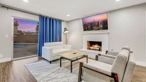 Uma sala de estar com sofá branco, mesa de centro, lareira e uma pintura da paisagem urbana na parede.