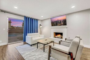 Una sala de estar con un sofá blanco, una mesa de centro, una chimenea y un cuadro de un paisaje urbano en la pared.