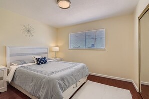 A bedroom with a bed, nightstands, a lamp, a window with blinds, and a ceiling light.