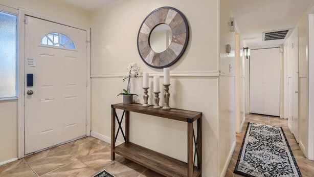 A hallway with a white door, a console table with candles, a wall clock, and a patterned rug. - Cheerful Home with Game Room! 10 Min to Strip! (Las Vegas)