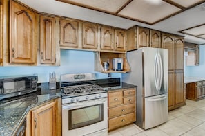 A kitchen with wooden cabinets, a gas stove, a microwave, and a stainless steel refrigerator.