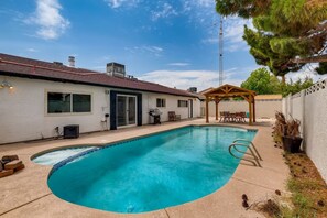 A backyard with a swimming pool, a covered patio, and a house with a white exterior.