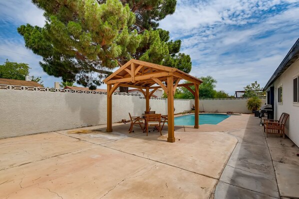 Un patio couvert avec une piscine, une pergola en bois et du mobilier d’extérieur.