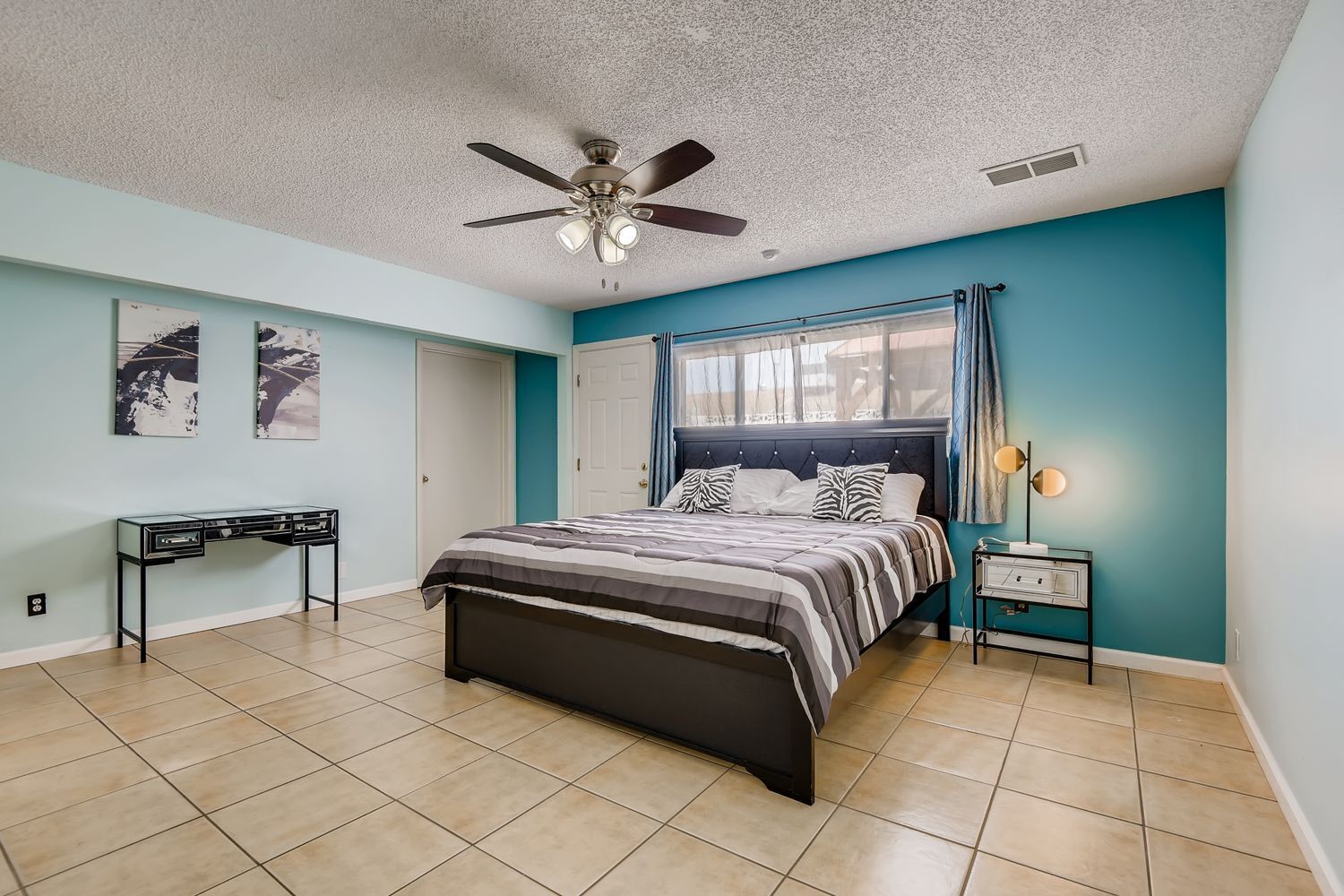 A bedroom with a bed, a desk, a ceiling fan, and a nightstand.
