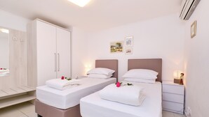 A hotel room with two beds, a wardrobe, a nightstand, and a wall-mounted air conditioner.