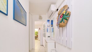 A hallway with white walls, a white door, and a white radiator. There are framed pictures on the wall and a small potted plant on the radiator.