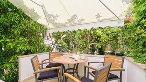 A round table with four chairs, surrounded by lush greenery and a white canopy.