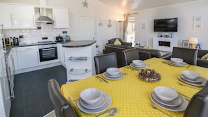 Une cuisine moderne avec des meubles blancs, un coin repas avec une nappe jaune et un téléviseur fixé au mur.