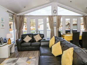 Ein Wohnzimmer mit einem schwarzen Ledersofa, einem kleinen Tisch mit einer Lampe und Blick auf eine Terrasse und Häuser durch große Fenster.