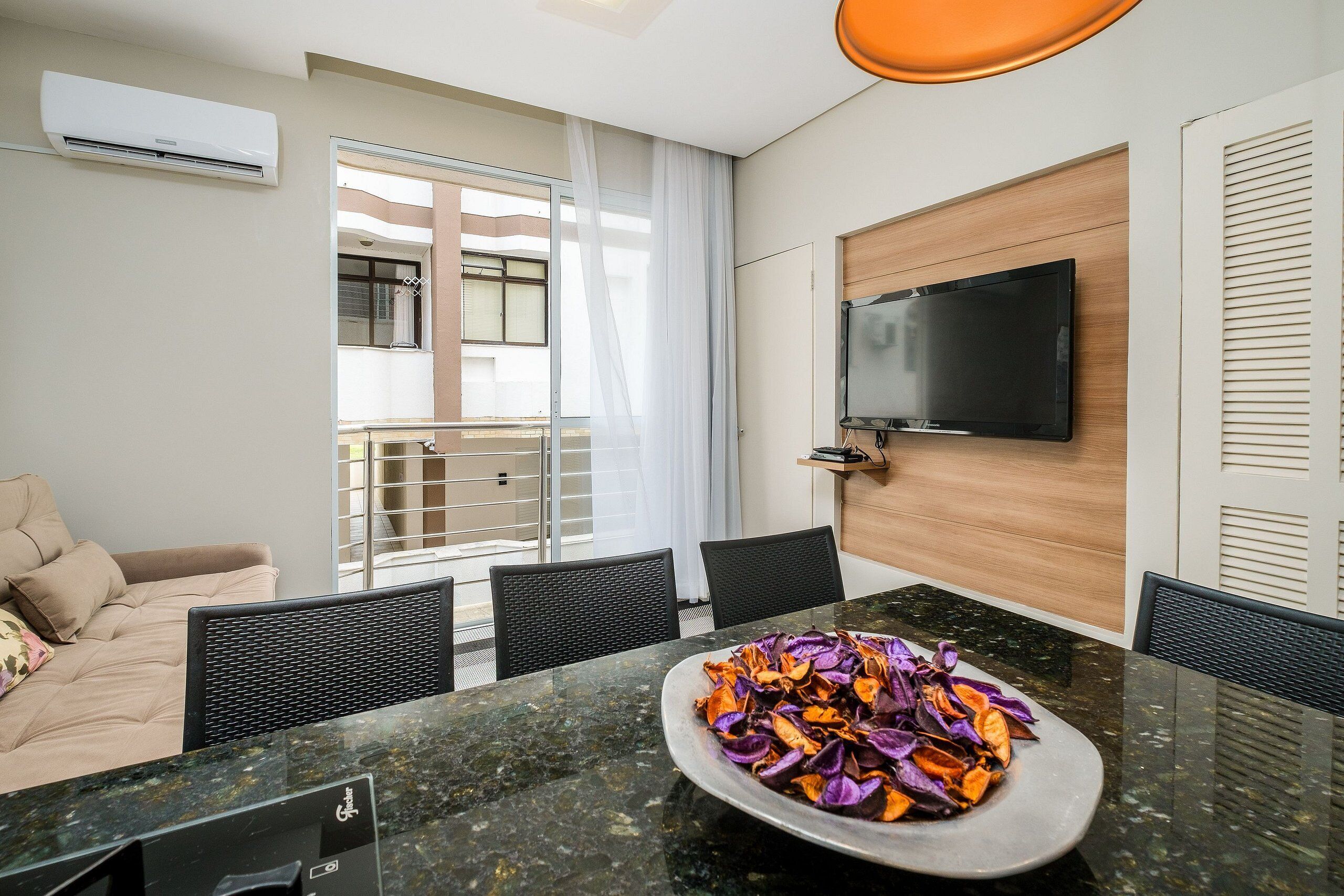 Une chambre d’hôtel moderne dotée d’un coin repas, d’un téléviseur à écran plat fixé au mur et d’un balcon avec une porte coulissante.