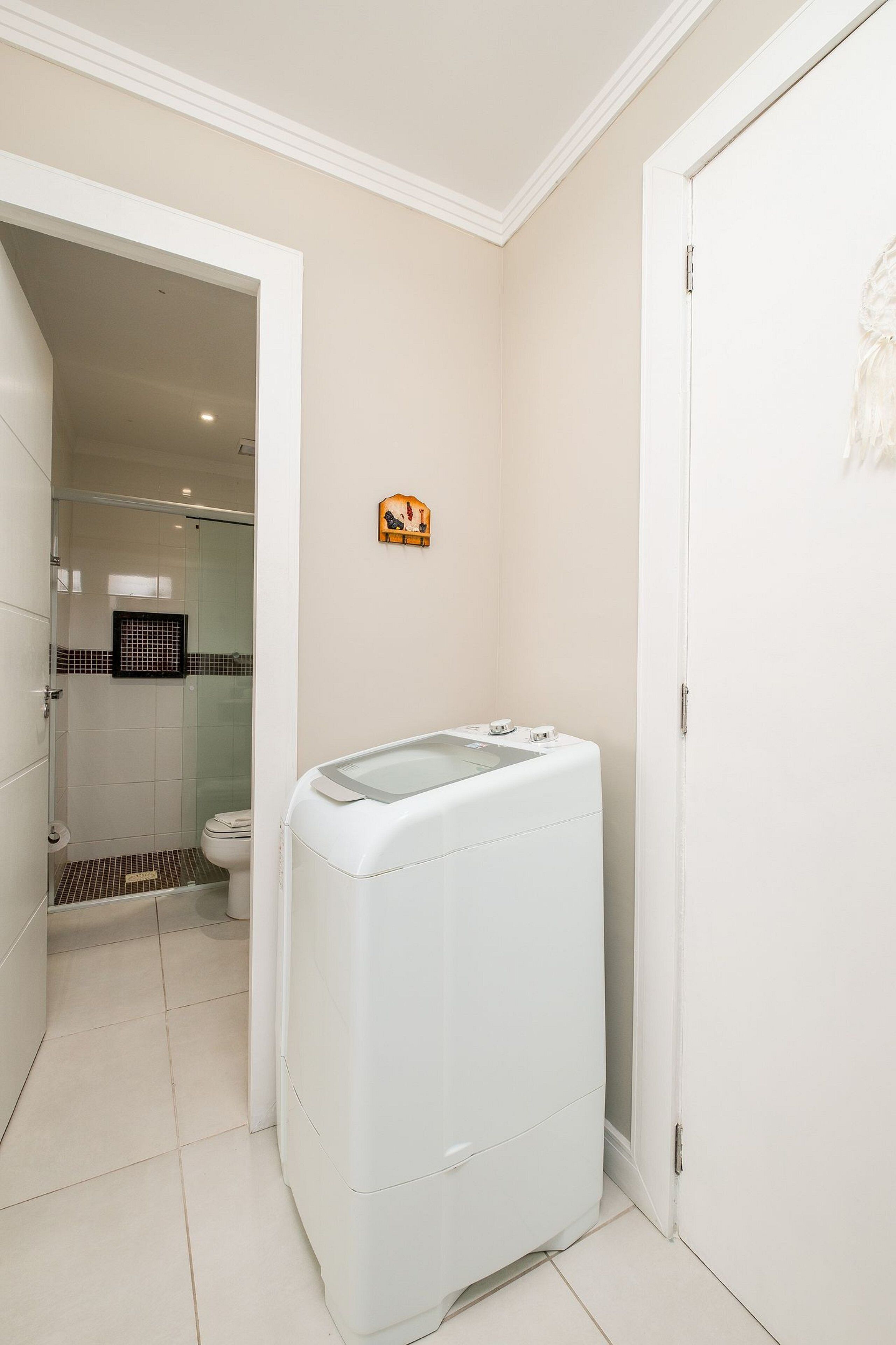 A laundry room with a washing machine, a toilet, and a shower area.