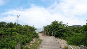 A wooden pathway leading to a beach, surrounded by greenery and a clear sky.