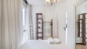 A modern bedroom with a large bed, a wooden ladder, a small shelf with plants, and a mirror.