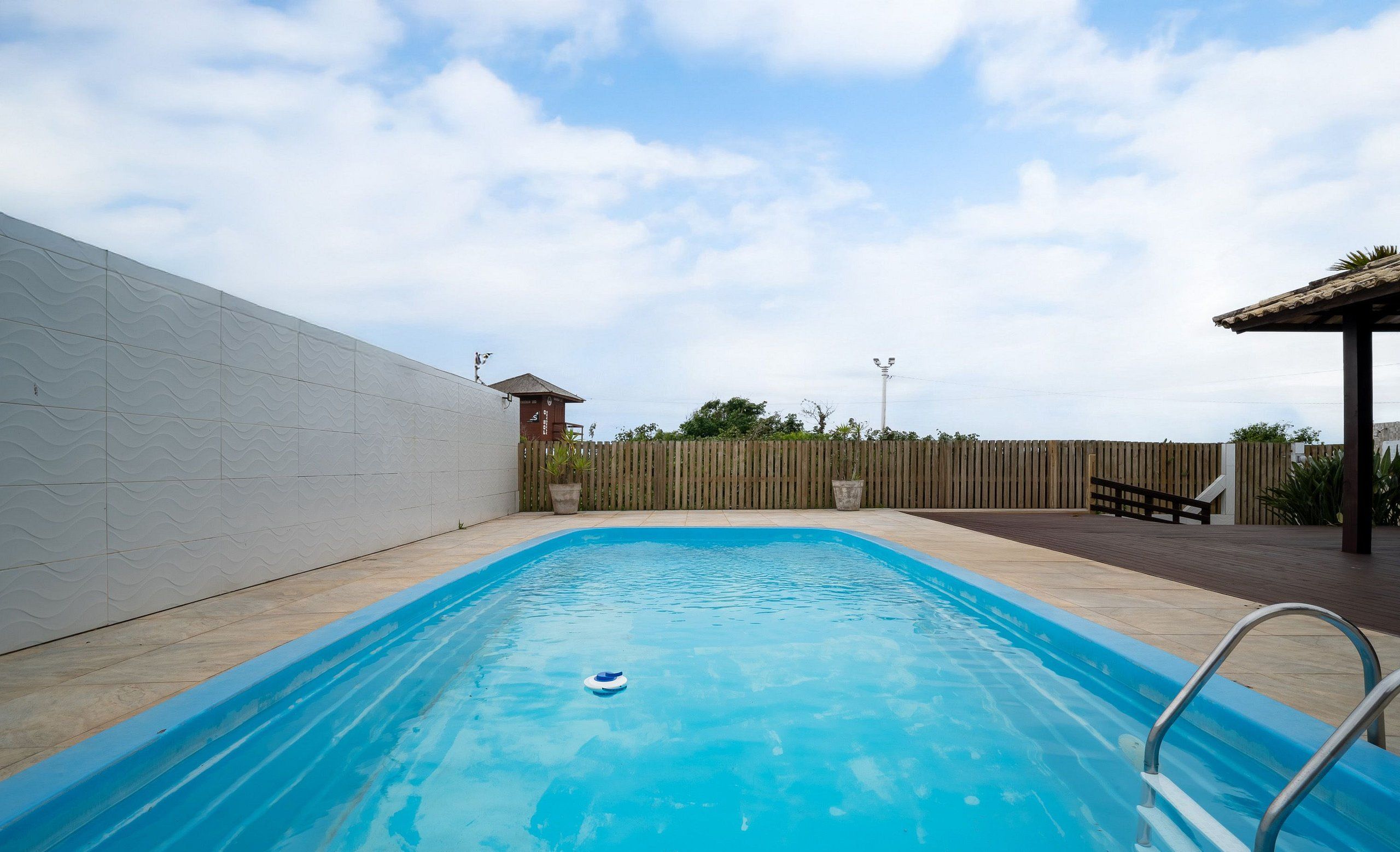 A rectangular swimming pool with a clear blue water surface, surrounded by a wooden deck and a low brick wall.