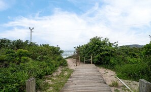 A wooden pathway leading to a beach, surrounded by greenery and a clear sky. - Oceanfront Condo With Pool in Floripa - IDA (Florianópolis)