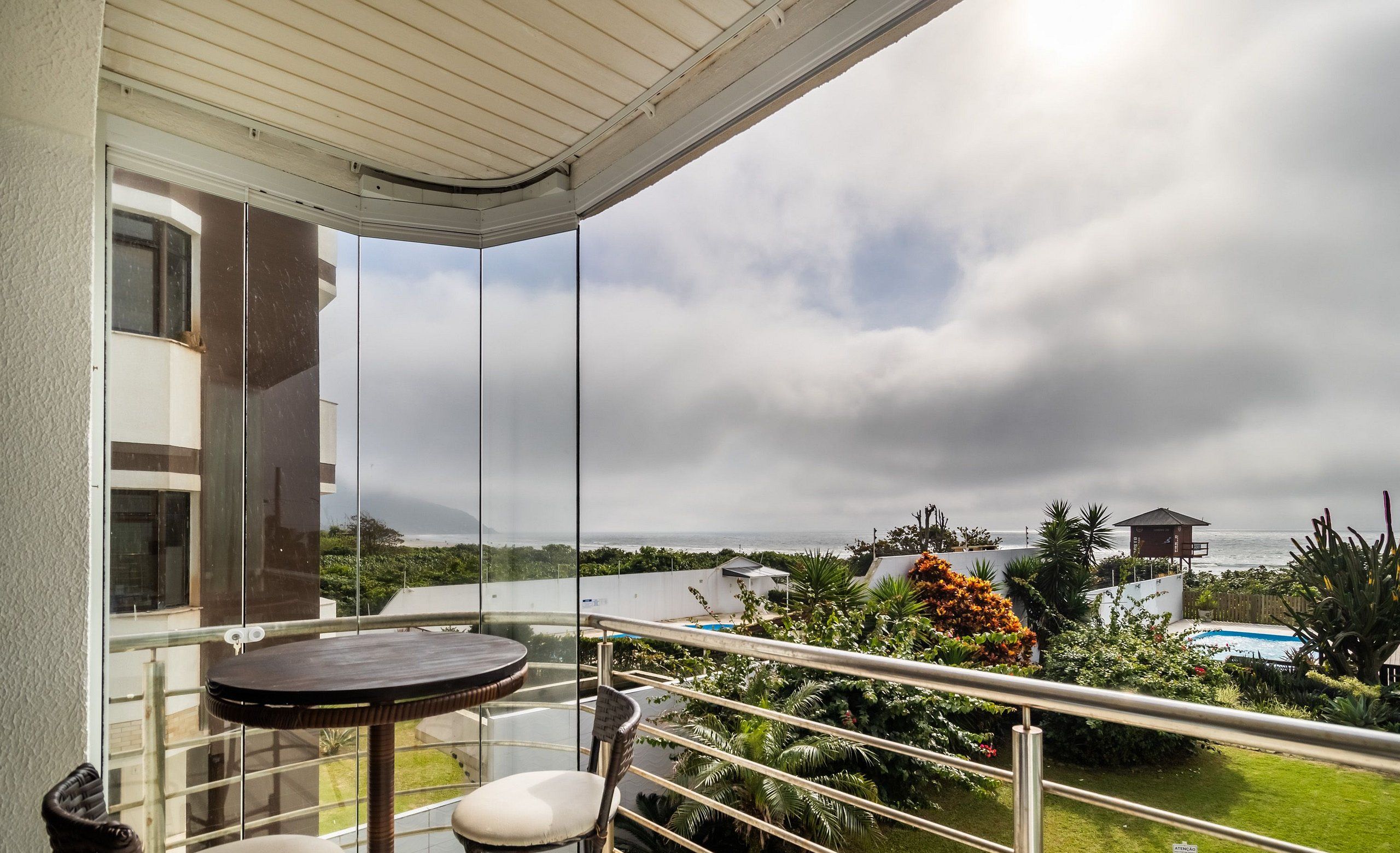 A balcony with a table and chair, overlooking a pool and greenery.