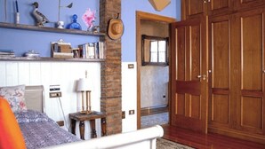 A bedroom with a bed, a bedside table, a lamp, a shelf with books and decorative items, and a wooden wardrobe. - Birds Junior Suite (Mungia)