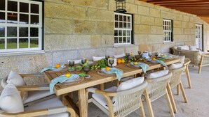 Un espace de restauration extérieur aux murs de pierre, avec une table en bois pouvant accueillir six personnes, des chaises en osier et une lanterne suspendue.