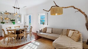Un coin repas comprenant une table ronde et des chaises, un canapé, un grand miroir et un luminaire suspendu.