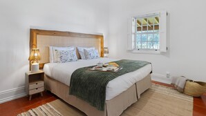 Une chambre à coucher avec une tête de lit en bois, deux tables de chevet avec des lampes, une fenêtre donnant sur un beau paysage et un plaid vert sur le lit.