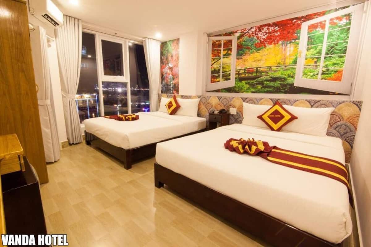 A hotel room with two beds, a window with a city view, and a painting on the wall.