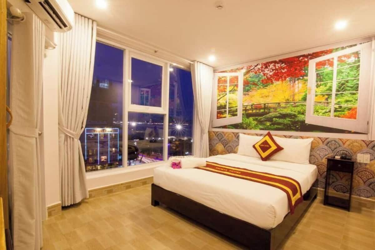 A hotel room with a large bed, a city view through the window, and a colorful mural on the wall.