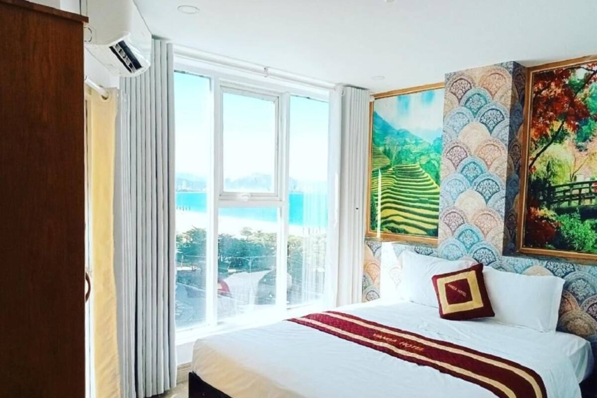 A hotel room with a large bed, a view of the city, and a painting on the wall.