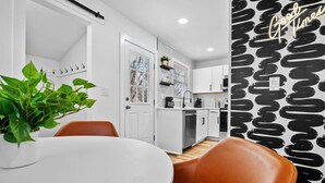 A modern kitchen with white cabinets, a black backsplash, and a dining area with a white table and brown chairs.