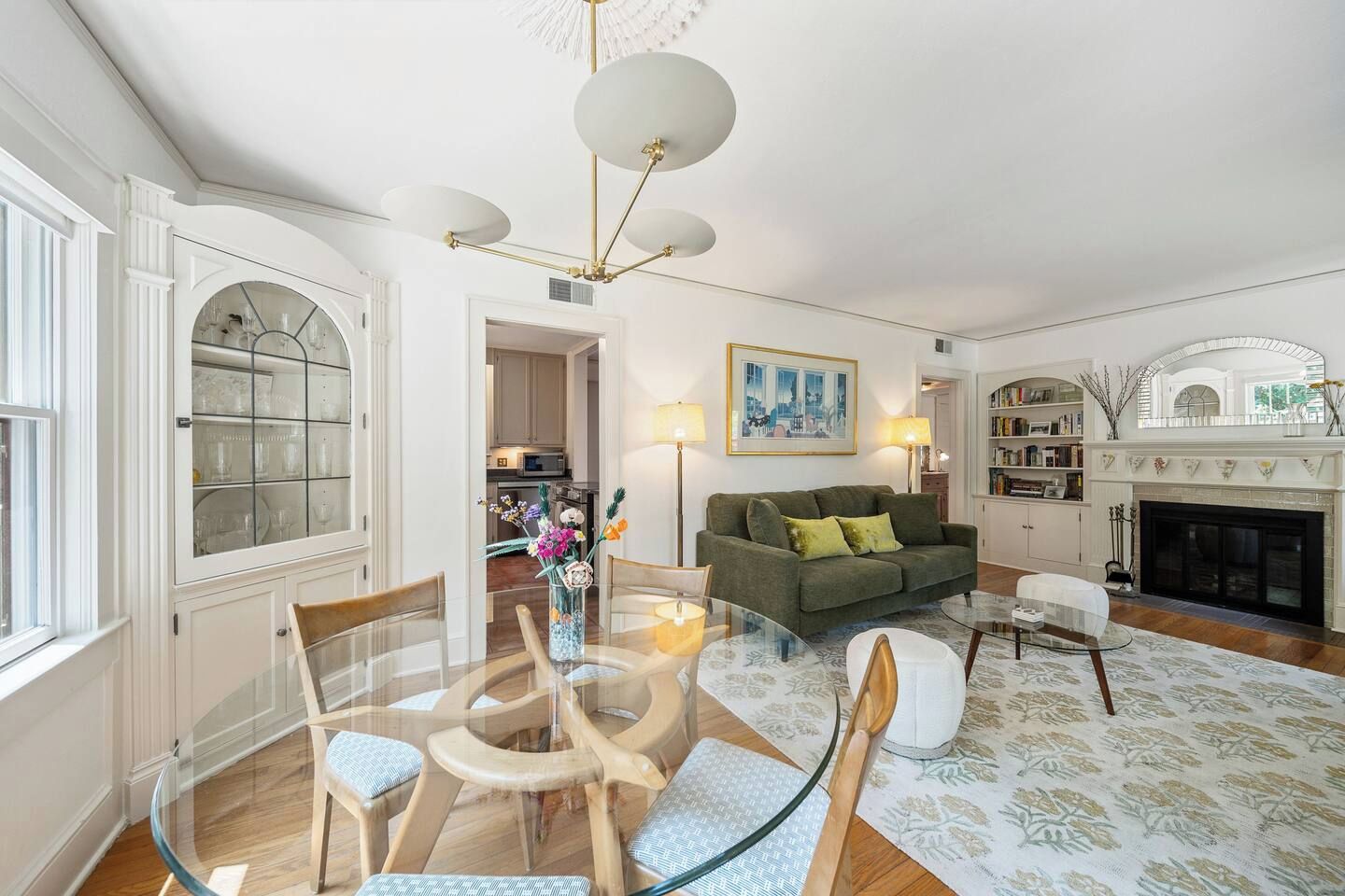A living room with a glass table, chairs, a sofa, a fireplace, and a bookshelf.